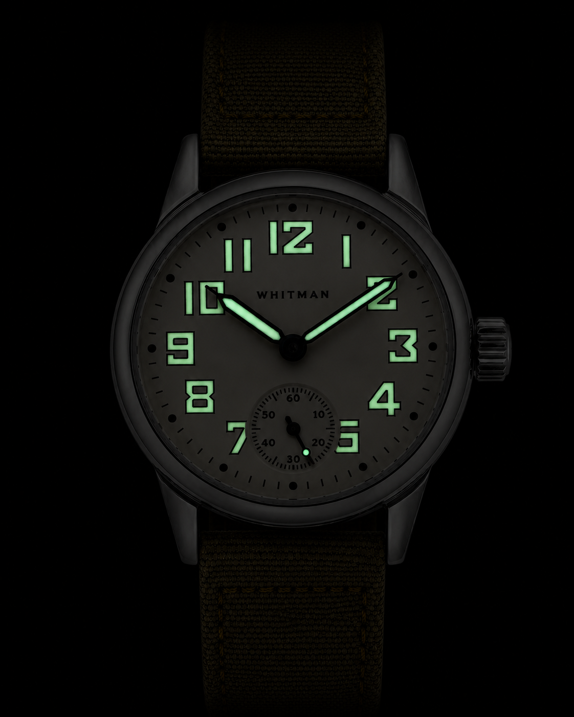 A WWII Ordnance Department wristwatch with a silver stainless steel case, an off-white dial with black Arabic numerals and hands, and an olive green canvas strap, shown in a low light environment to show the illuminated dial.